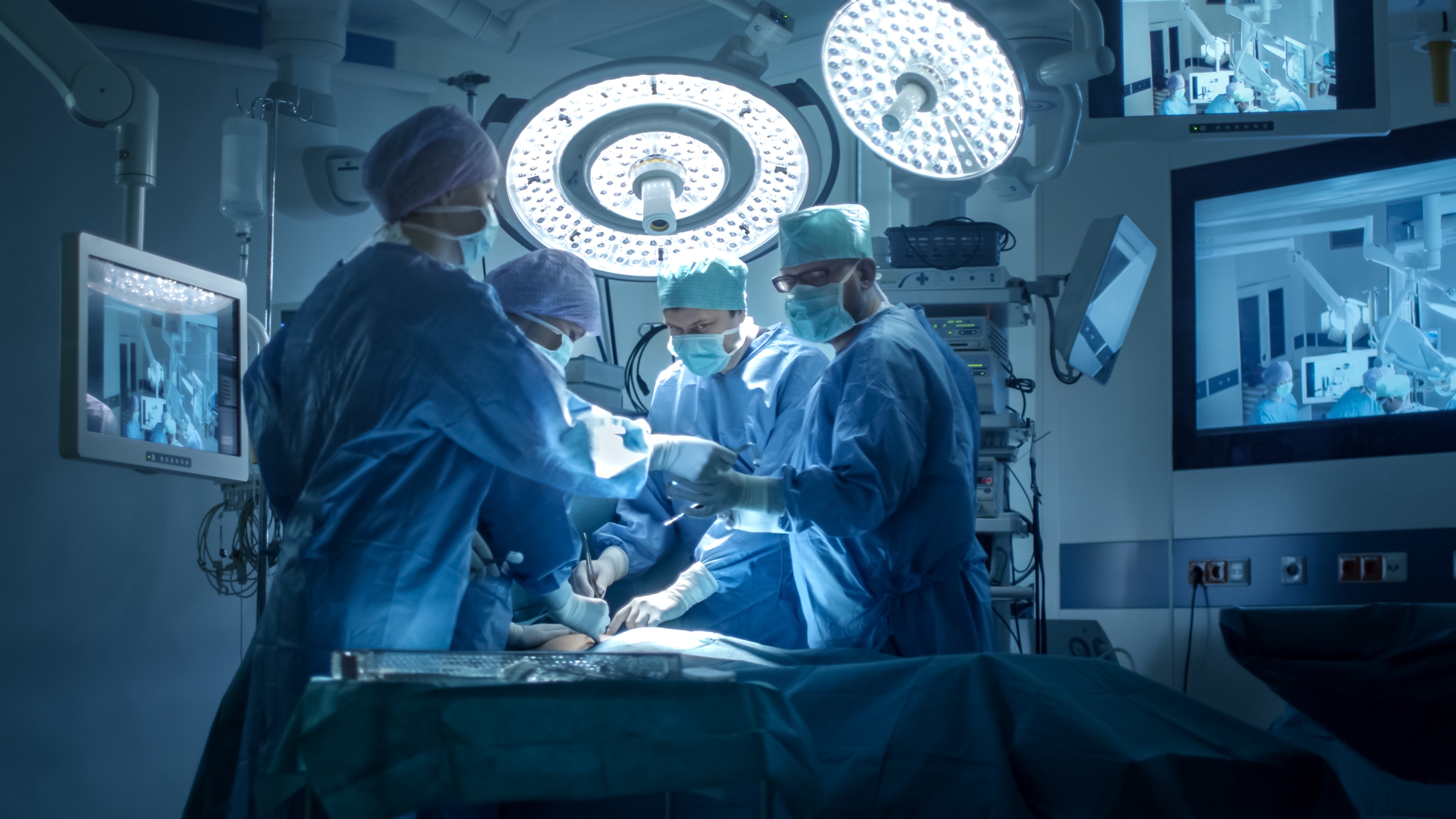 Surgical team performing an operation in a high-tech operating room, focused under bright lights and surrounded by medical monitors
