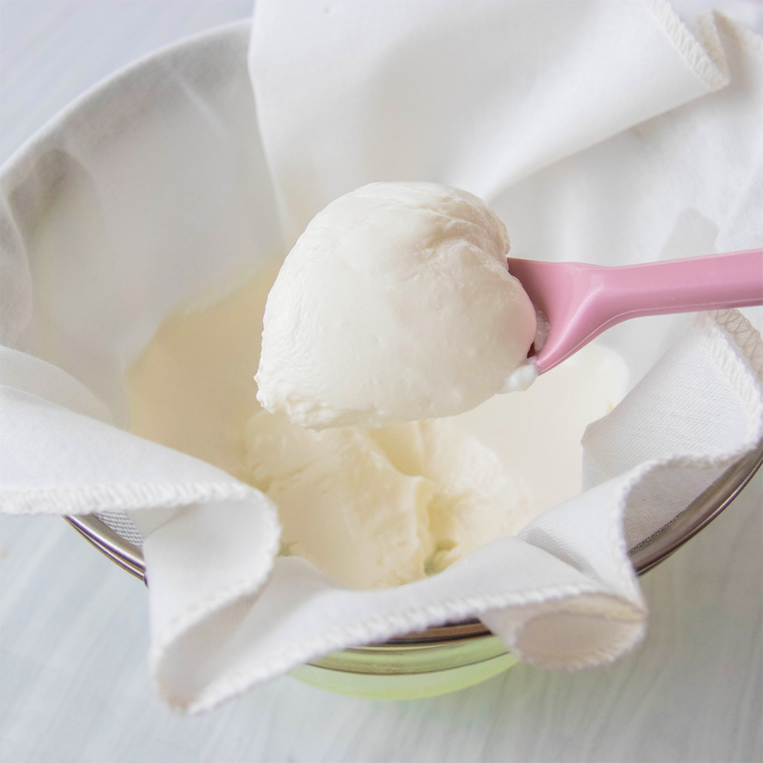 ボウルに置かれた布の上に、水切したヨーグルトがスプーンですくわれている。