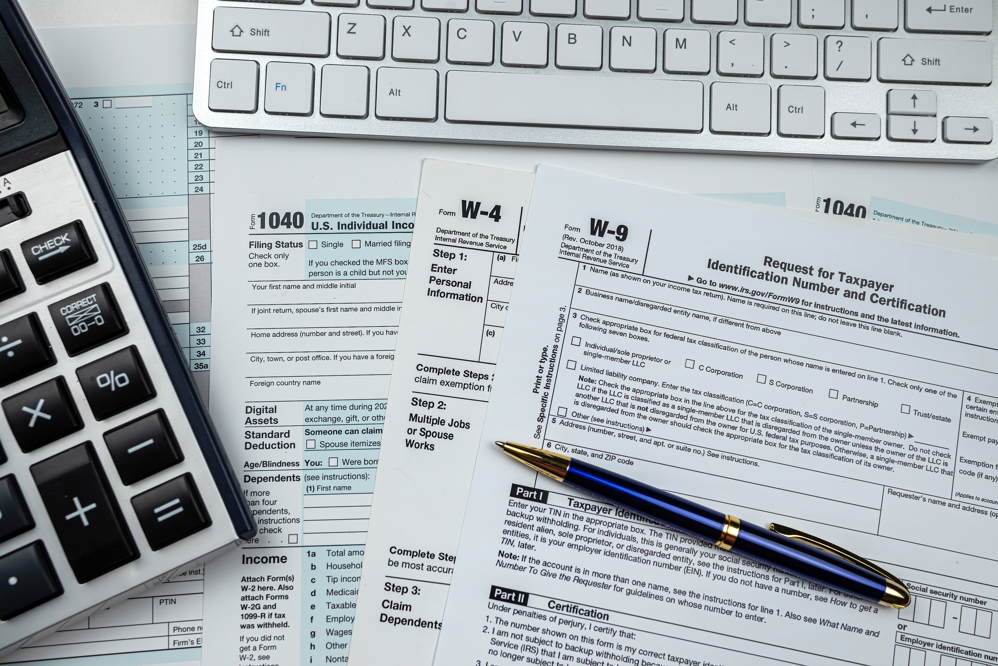 Tax forms W-4 and W-9 are spread on a desk, alongside a keyboard and calculator, suggesting a focus on financial or tax-related tasks