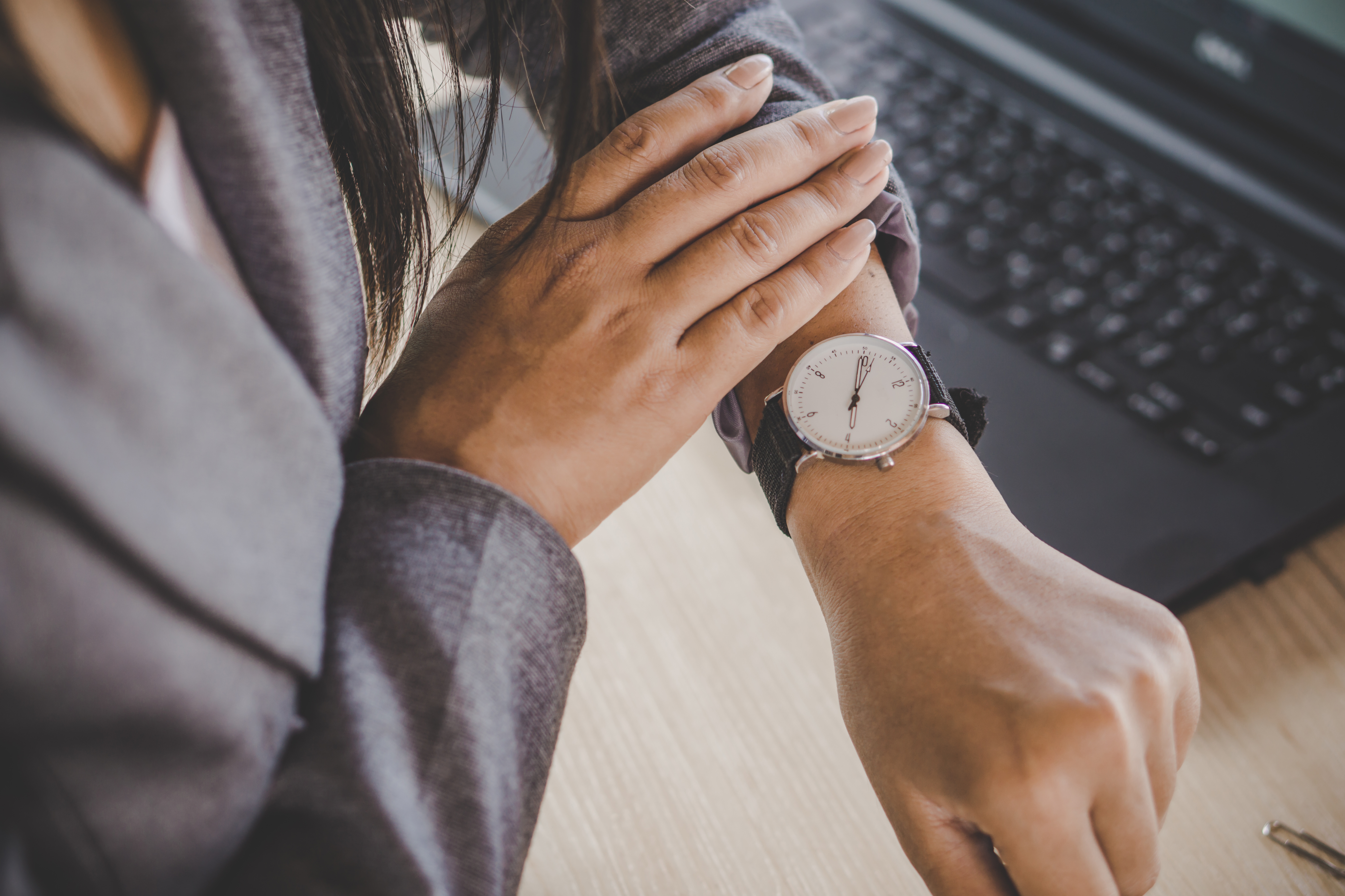 Person in a suit looking at their wristwatch while working on a laptop