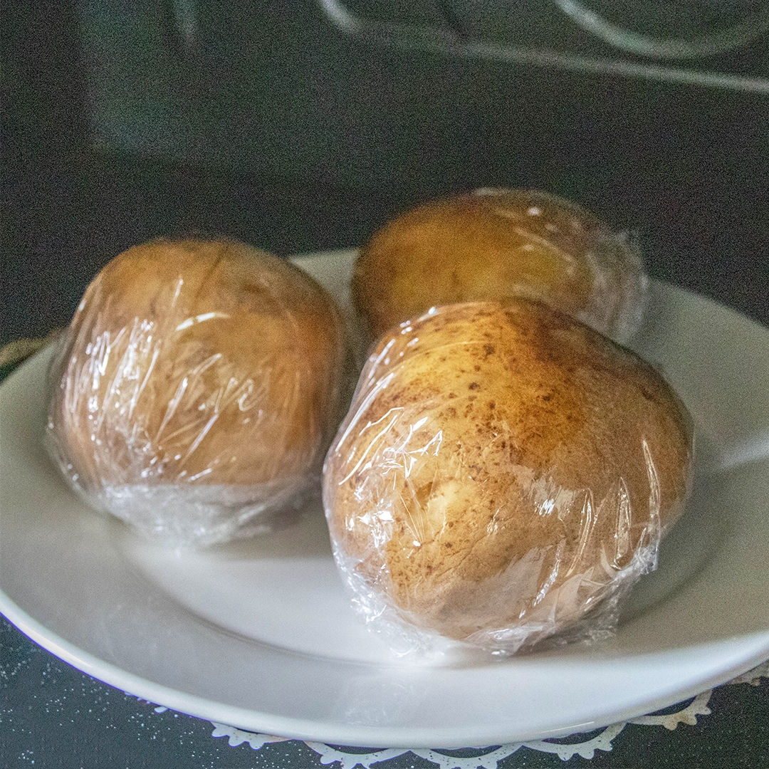 皿にのったラップで包まれた3個のじゃがいも。レンジで加熱する様子。