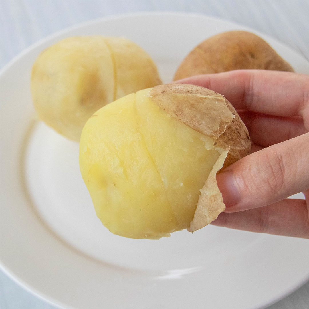 手で持たれた皮の一部がむけた加熱されたじゃがいもが皿にある。