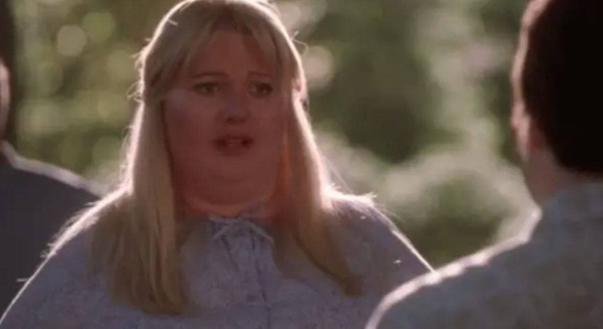 A person with long blonde hair looks surprised or concerned while speaking to someone outside