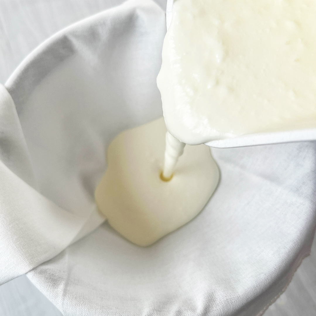 布巾をかけたザルにヨーグルトを注いでいる様子。ヨーグルトがろかされている過程。