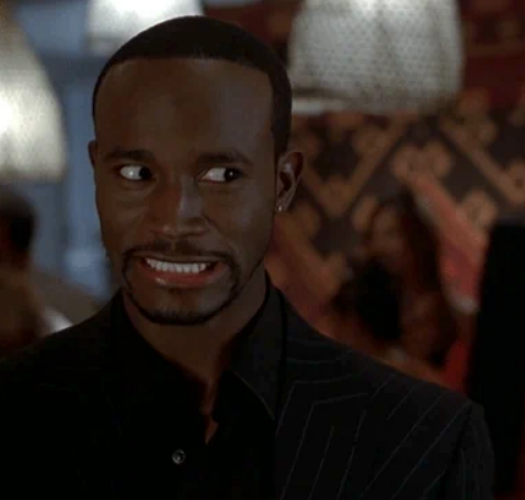 Smiling person in a dark suit with a tense expression, standing indoors, possibly reacting to a wedding moment