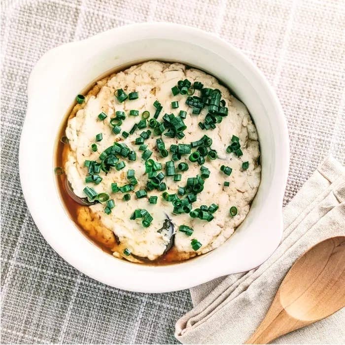 皿に盛られた豆腐料理、上にネギが散らされている。スープが添えられている。