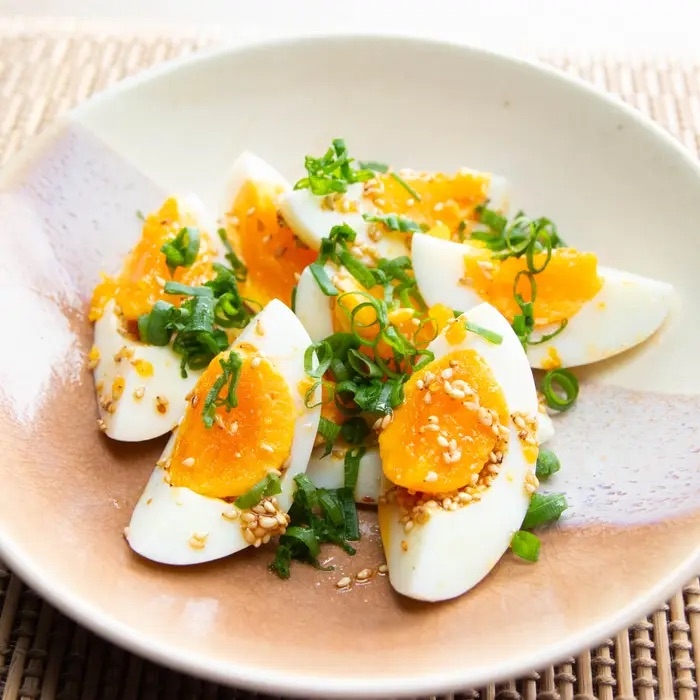 半熟卵のスライスにネギとゴマがトッピングされた料理が皿に盛られている。