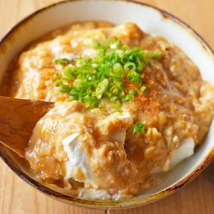 ネギと調味料でトッピングされた豆腐料理がボウルに入っており、スプーンで一口持ち上げられています。