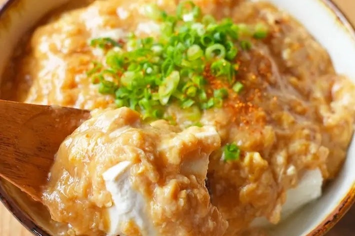 ネギがトッピングされた豆腐入りの中華風お粥が入ったボウル。スプーンでお粥をすくう。