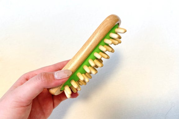 手に持たれた木製のマッサージ器。緑色の土台に丸い突起がついている。