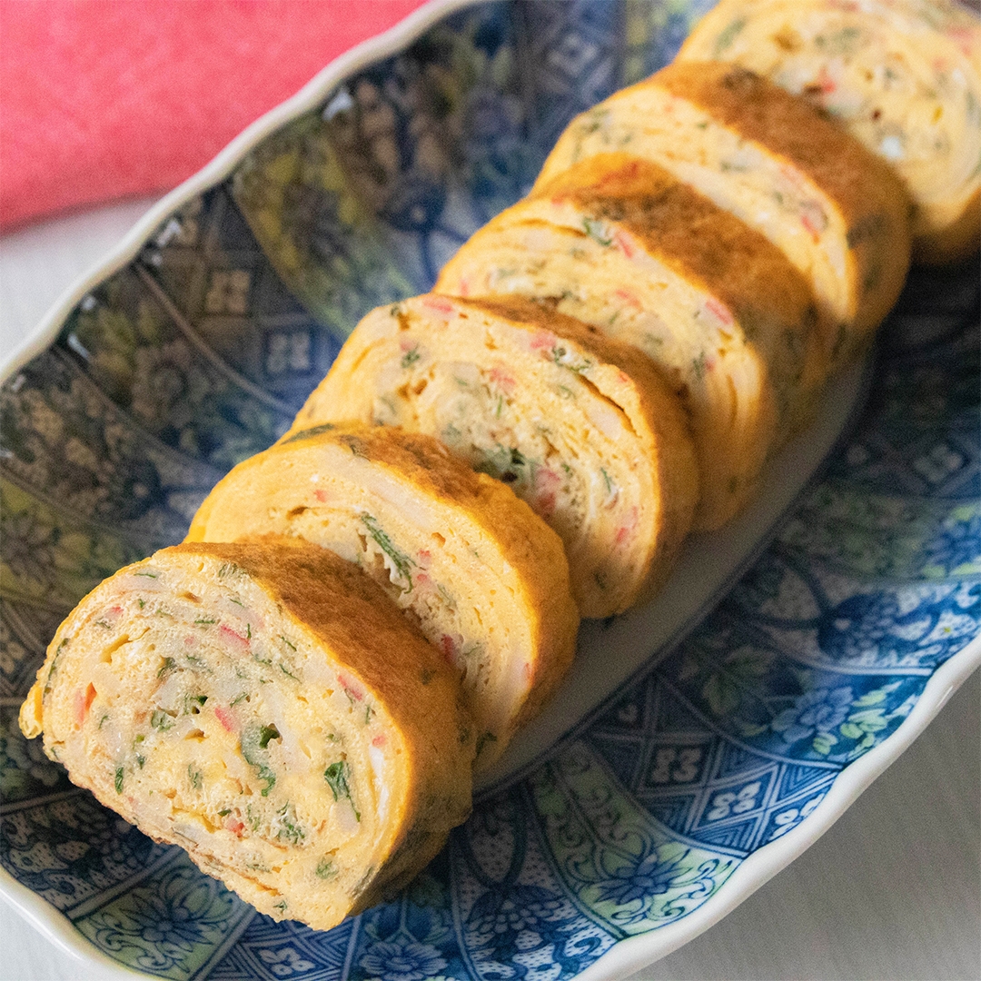 和食の青い模様の皿に盛られた卵焼き。卵焼きには大葉とカニカマが入っている。
