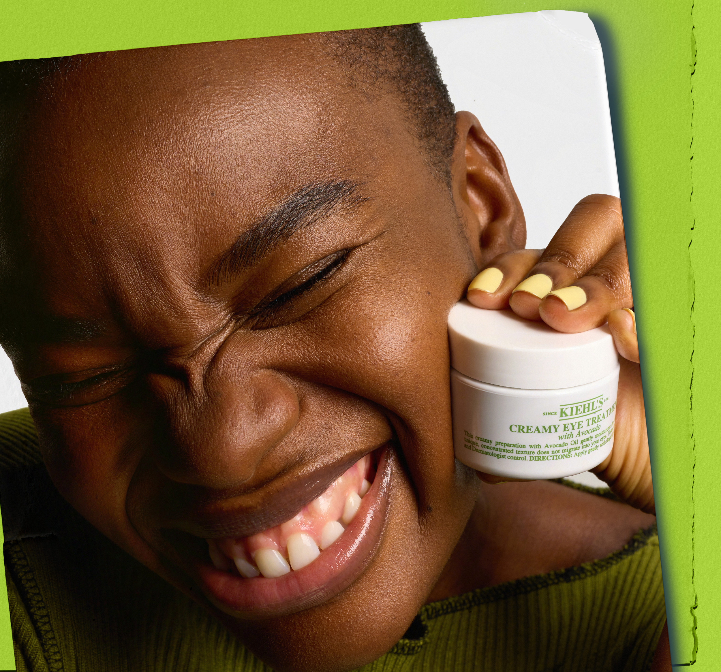 Person smiling broadly while holding a jar of creamy eye treatment near their face