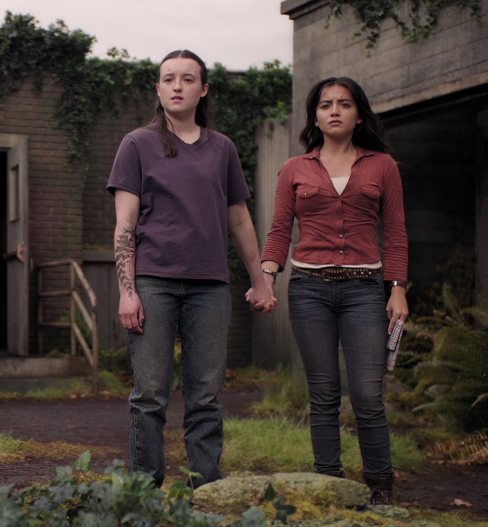 Ellie and Dina holding hands while looking in the distance