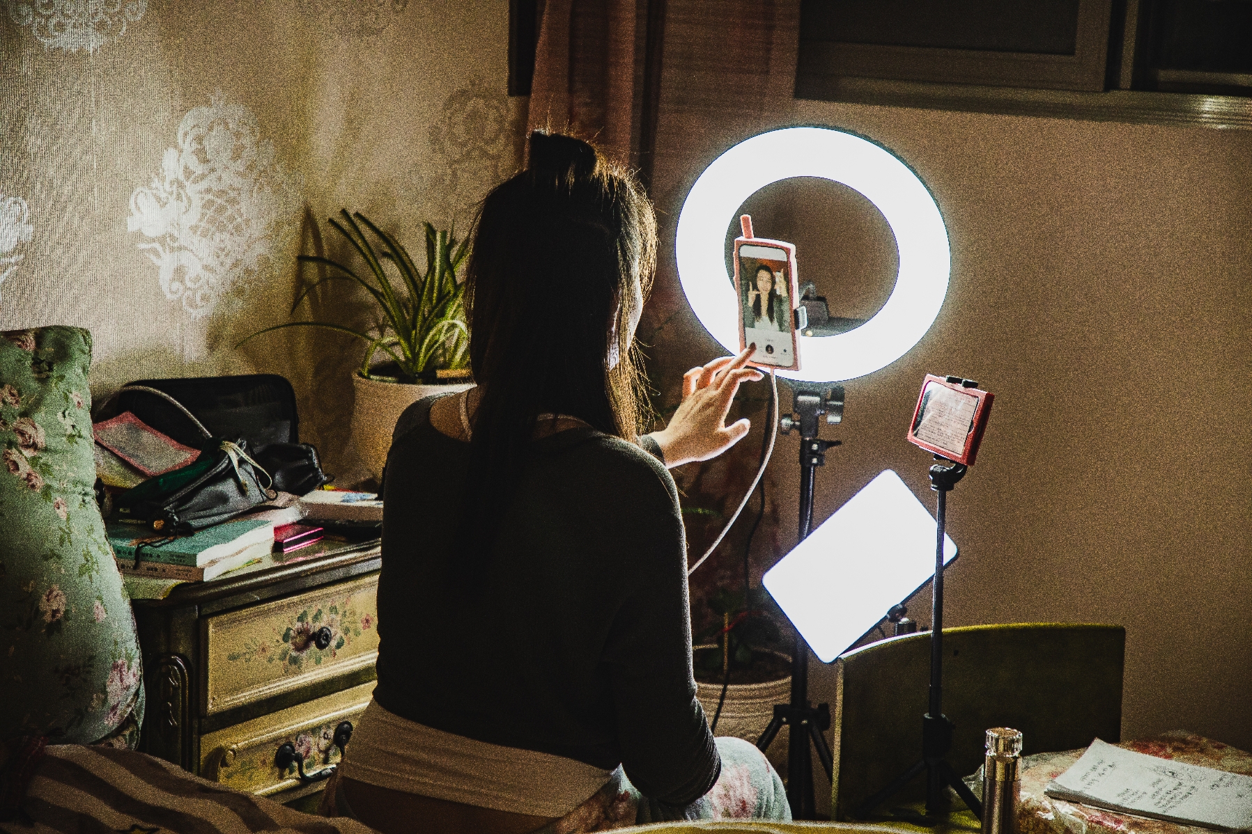 Person recording video in cozy room using smartphone and ring light