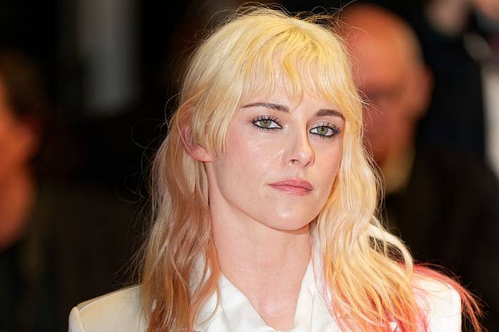 Person with long hair and bangs at a formal event, wearing a white outfit with an open collar