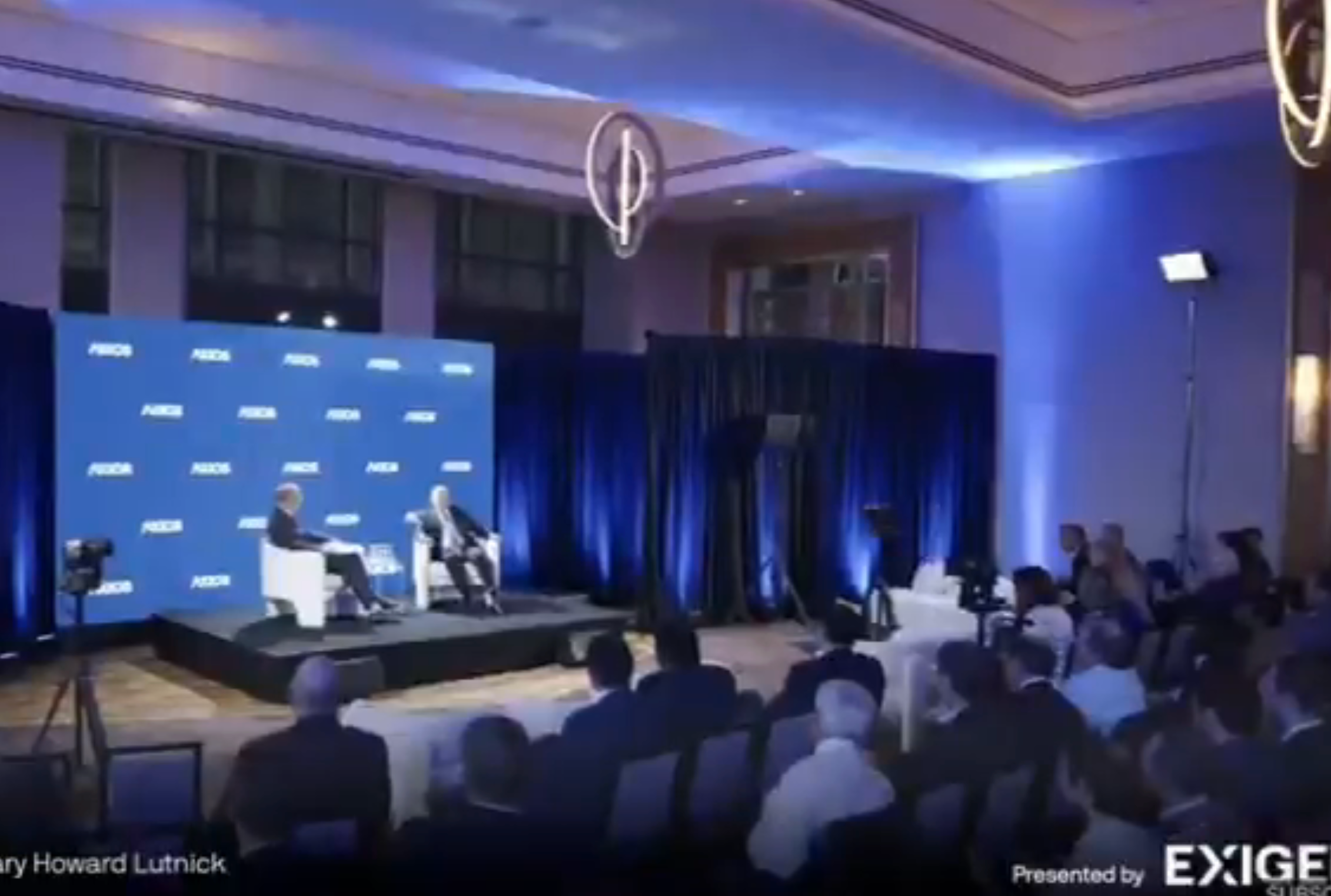 Two people are seated on stage for a panel discussion with an audience watching. Displays show &quot;ADIPEC.&quot;