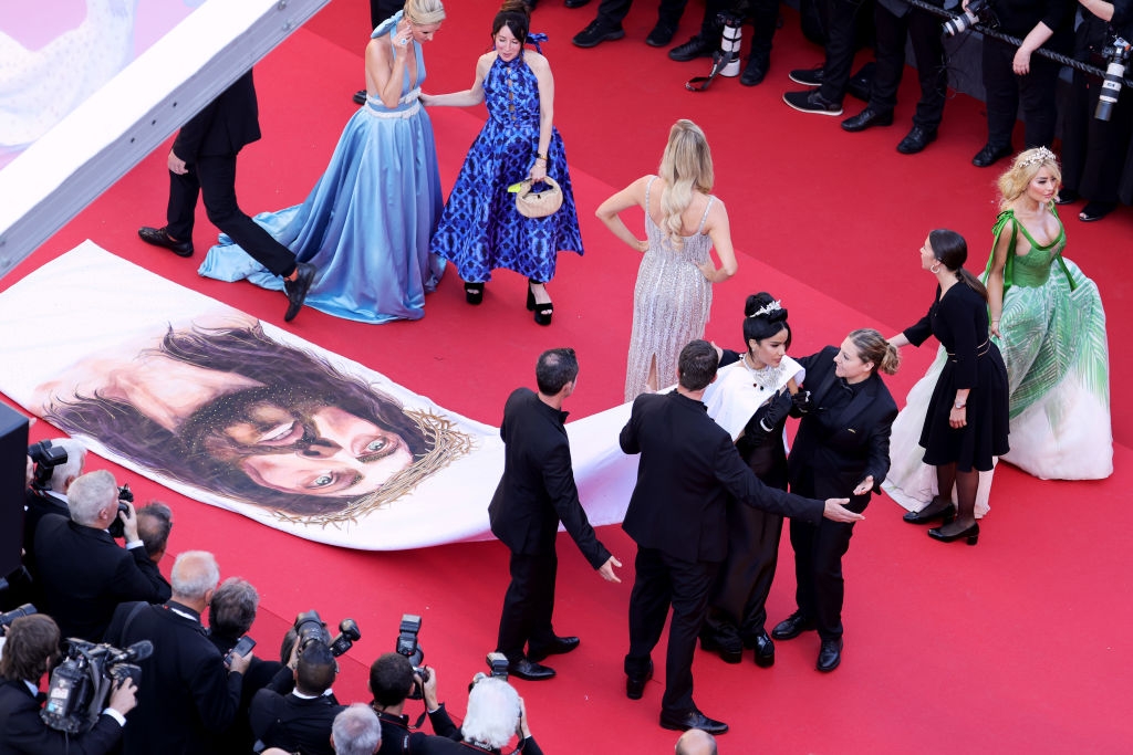 Person on red carpet in an intricately patterned gown with a long train, featuring floral and geometric designs