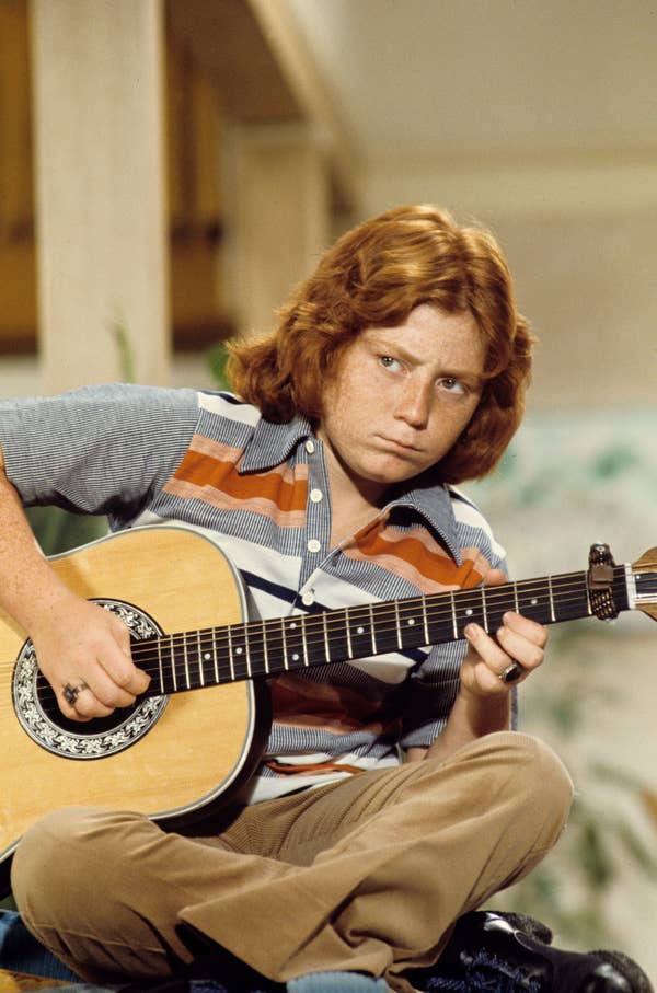 Person playing an acoustic guitar, wearing a striped shirt and engrossed in music