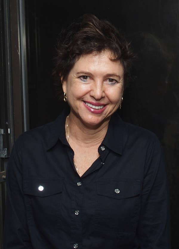 A woman wearing a buttoned shirt smiles at the camera