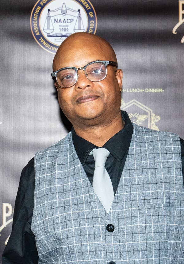 Person dressed in a plaid vest, black shirt, and tie at a formal event with "Power of Influence" signage in the background