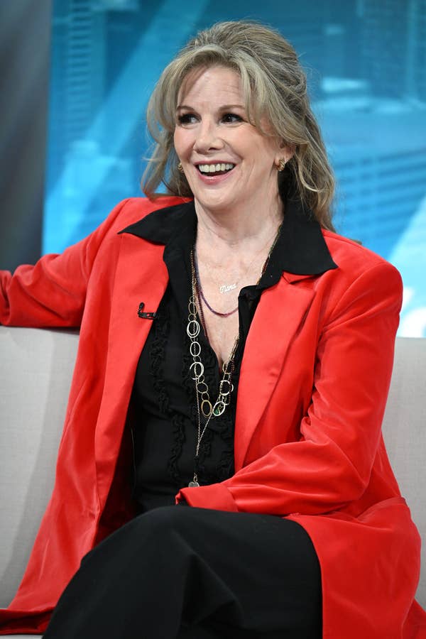 Person in a bright jacket and black shirt, seated and smiling during a televised interview