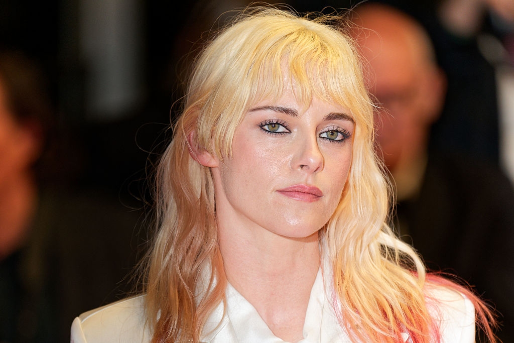 Person with light blonde hair in formal attire at an event, gazing subtly towards the camera