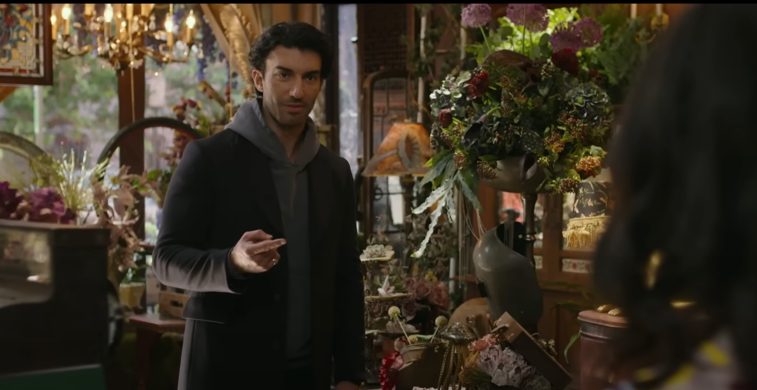 Man in a cozy store, surrounded by flowers and vintage items, looks inquisitively at someone outside the frame