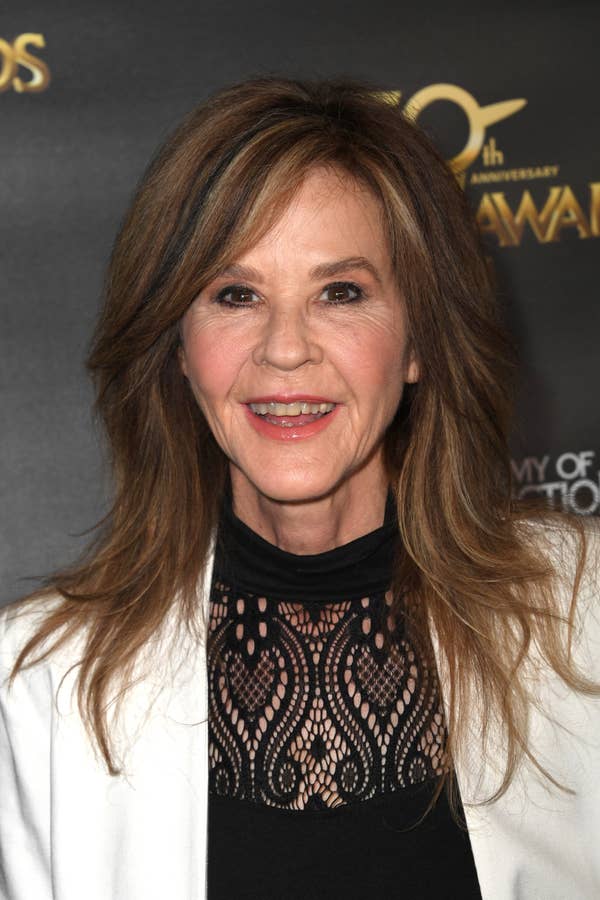 Person in stylish lace-top attire at an award event backdrop, smiling