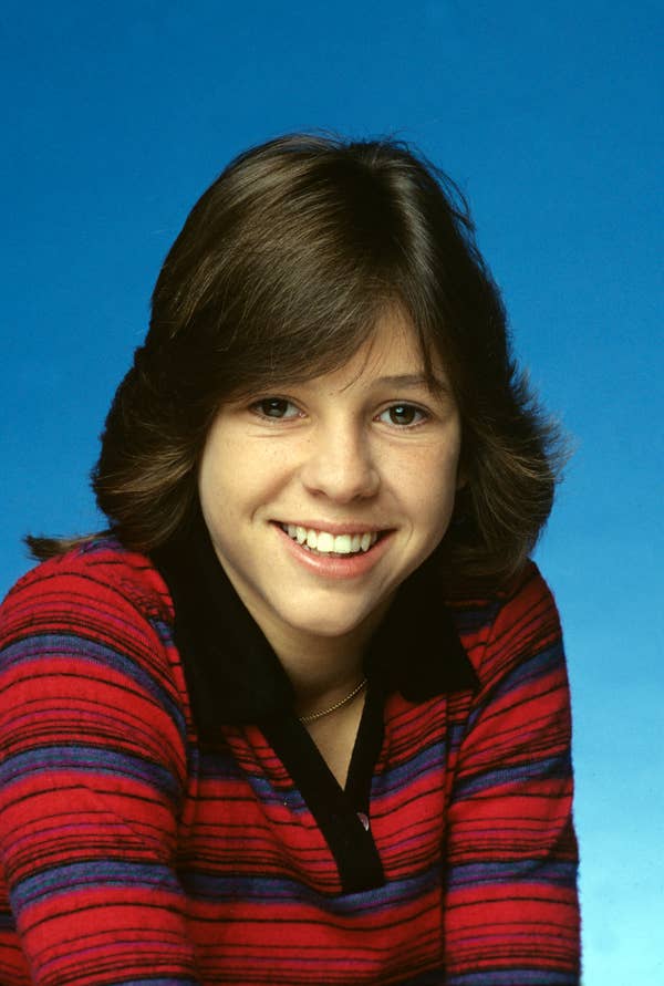 Smiling person with medium-length hair, wearing a striped top with a collar, set against a plain backdrop
