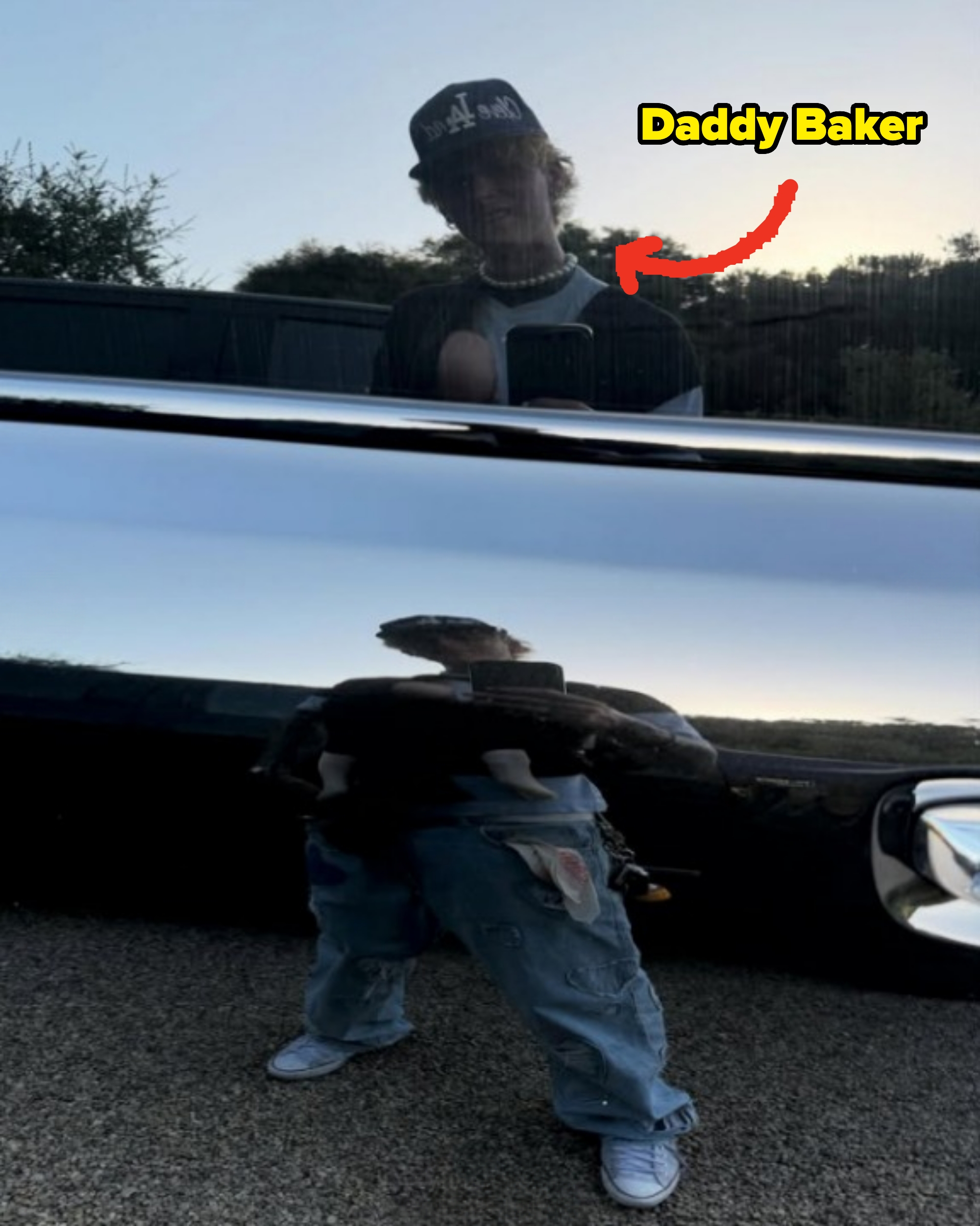 A person wearing a cap and casual clothes is reflected in a shiny truck surface, partially obscured. Natural landscape in the background