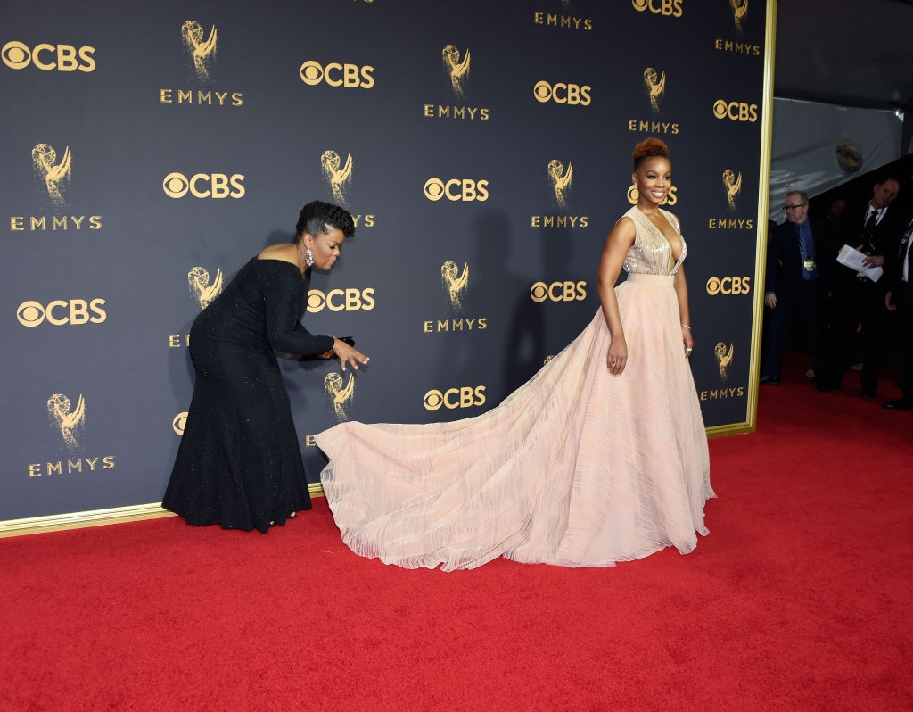 Yvette in a demure, understated gown, fixing the long train of Anika's elegant, flowing dress