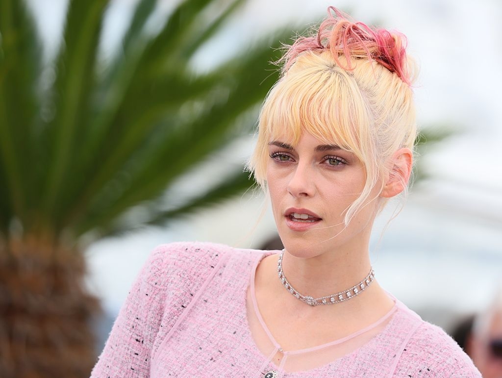 Person with short hair styled up, wearing a textured top and a choker necklace, posing outdoors