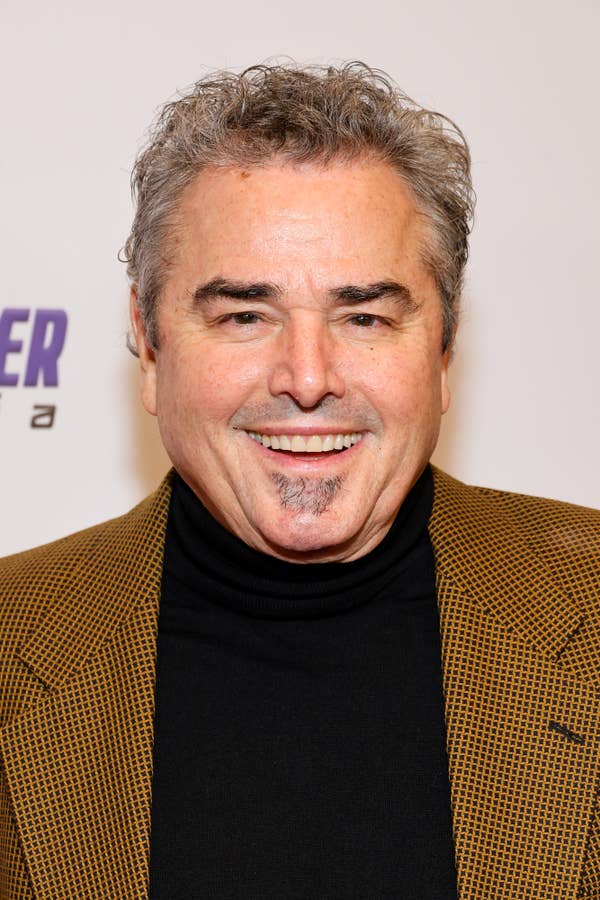 A man in a houndstooth blazer and black turtleneck smiles at a red carpet event