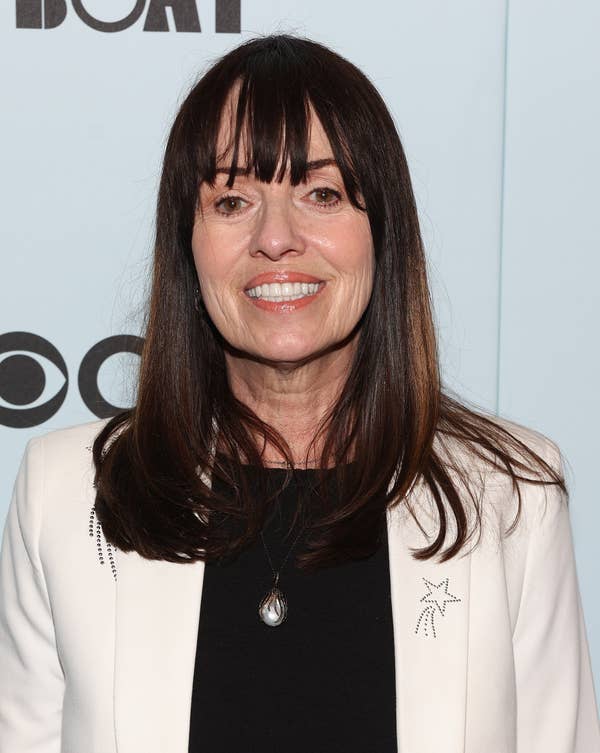 Person smiling on a red carpet, wearing a white blazer with star embellishments over a black top