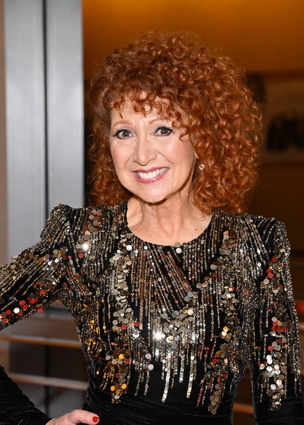 Person smiling in a sparkling, sequin-patterned dress at a formal event. Their curly hairstyle adds to the vibrant appearance