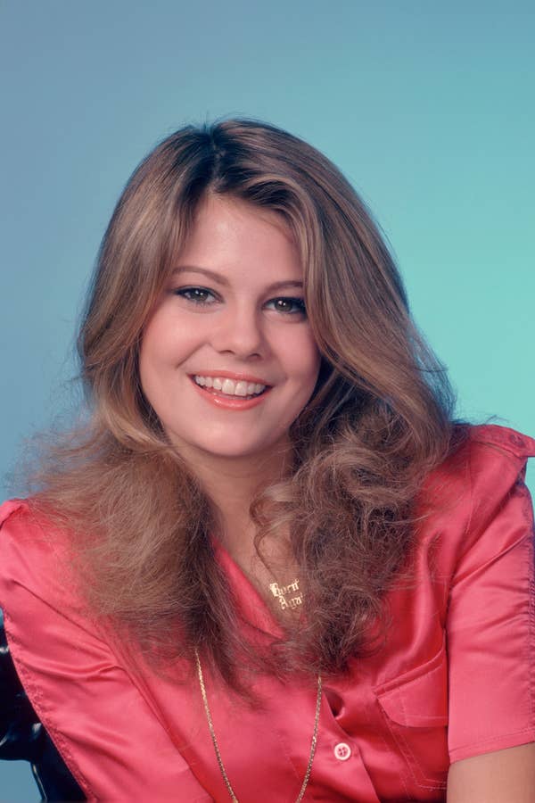 Person smiling, wearing a silky blouse with voluminous hair