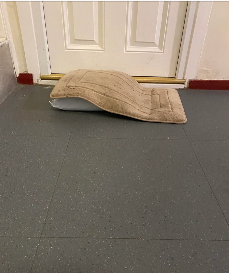 A door with a package bent in half under it, preventing the door from closing properly