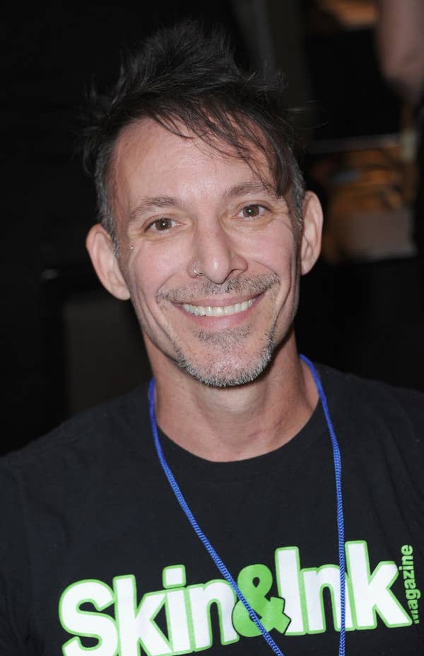 Person smiling at event, wearing a T-shirt with "Skin & Ink" written on it and a blue lanyard