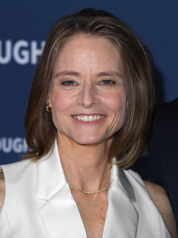 Person smiling in a formal white outfit at a celebrity event