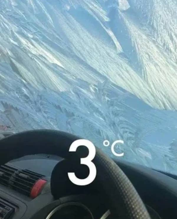 Frost-covered car windshield with a dashboard and steering wheel visible, displaying a temperature of 3 degrees Celsius