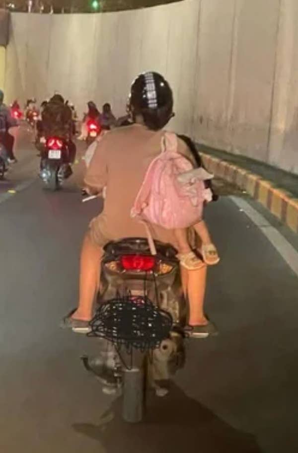 Person riding a scooter through a tunnel, carrying a passenger sitting on the back with a pink backpack