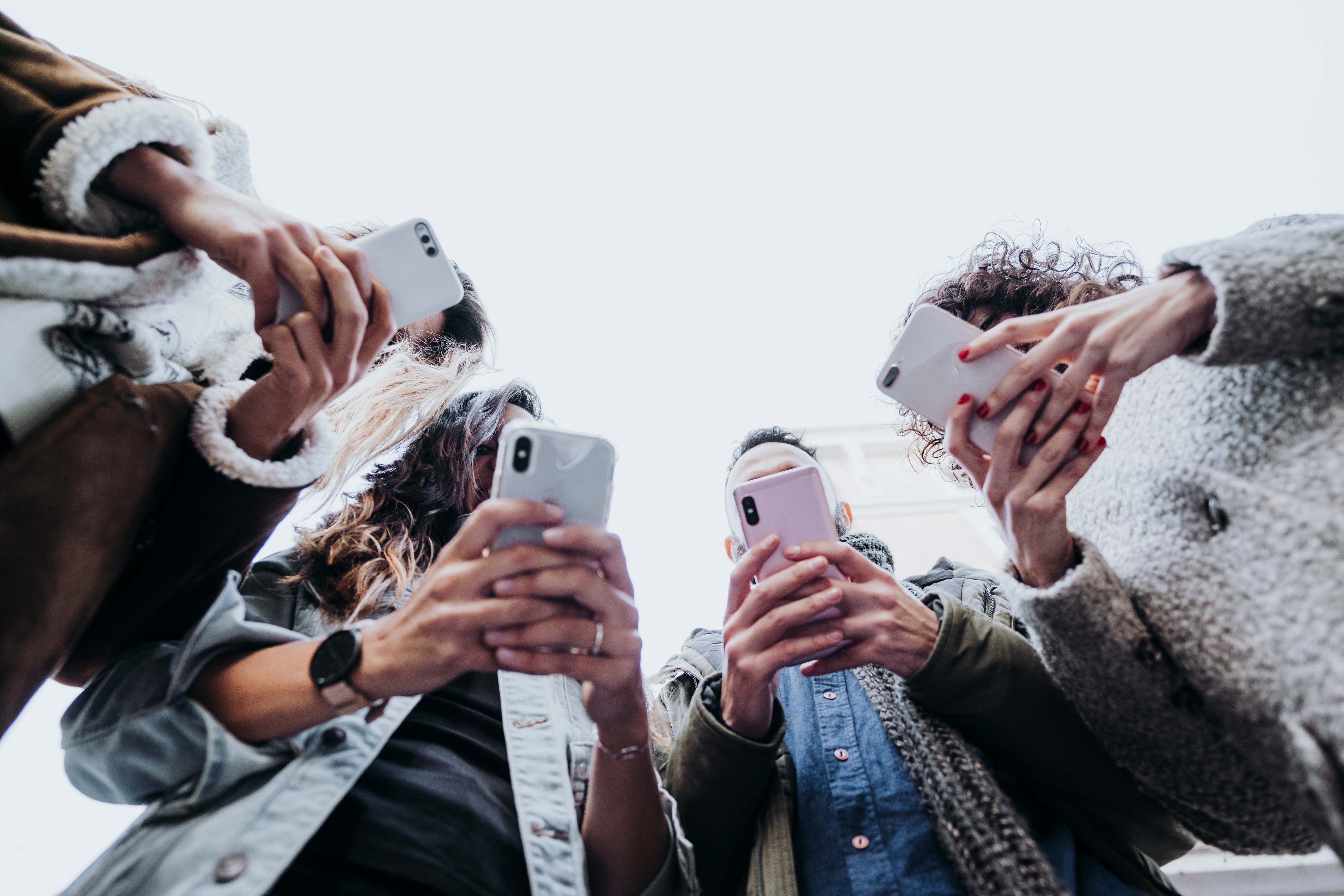 People holding smartphones, photographed from below, looking at screens