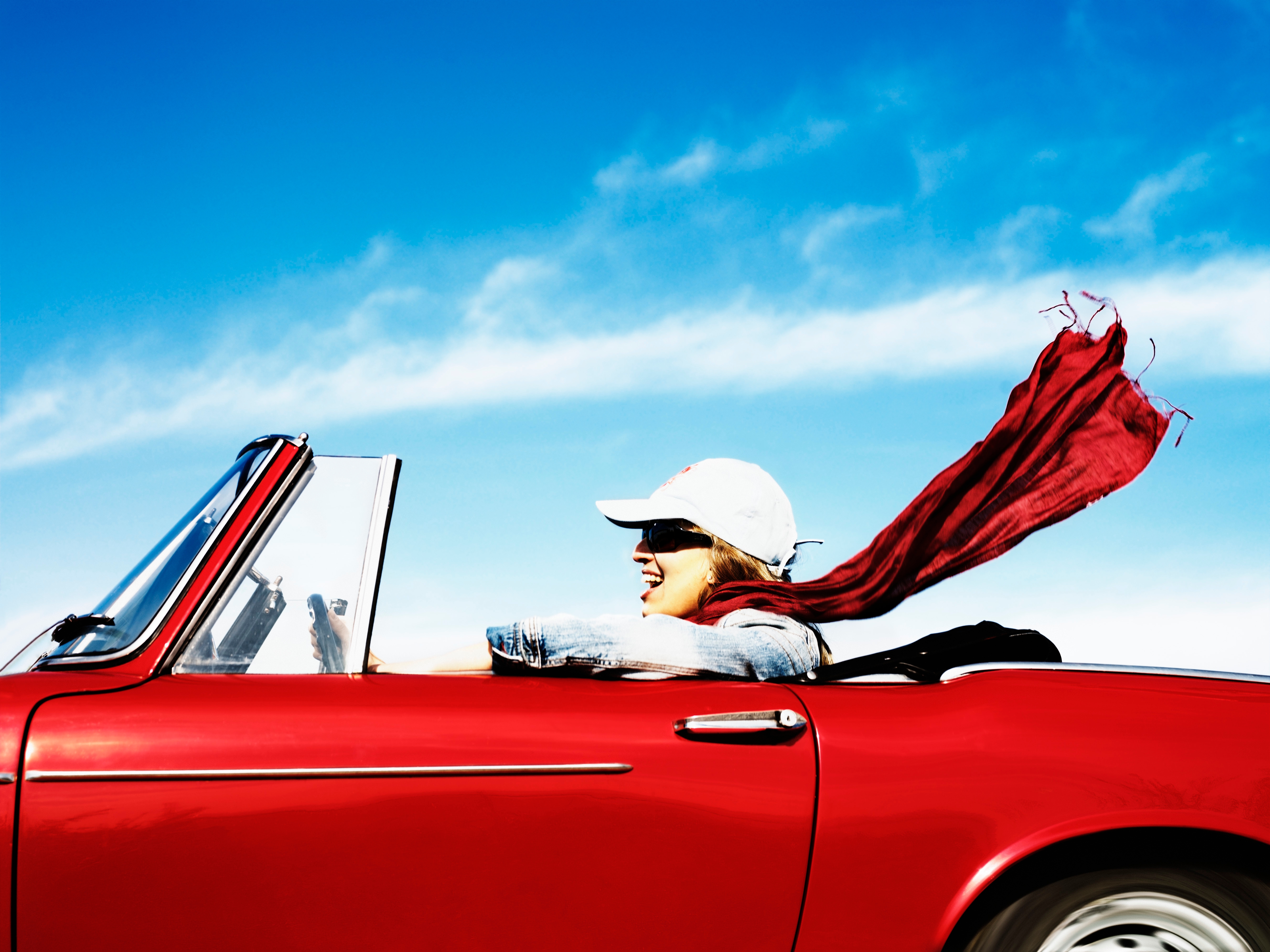 Person driving a convertible with the top down. Their scarf is blowing in the wind, creating a sense of freedom and adventure