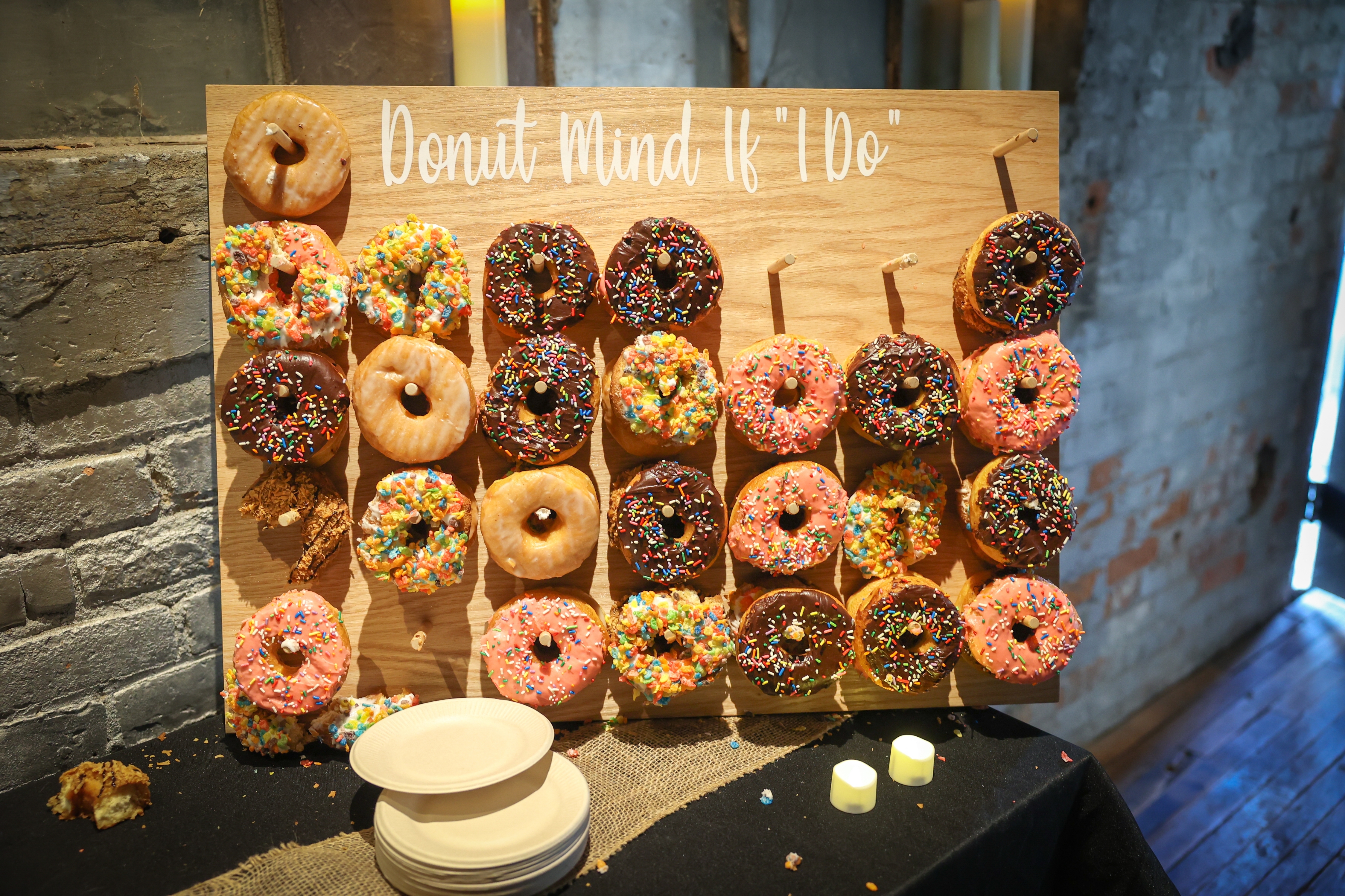 Wall display with assorted donuts and a sign reading "Donut Mind If 'I Do'," set up as a creative wedding dessert table