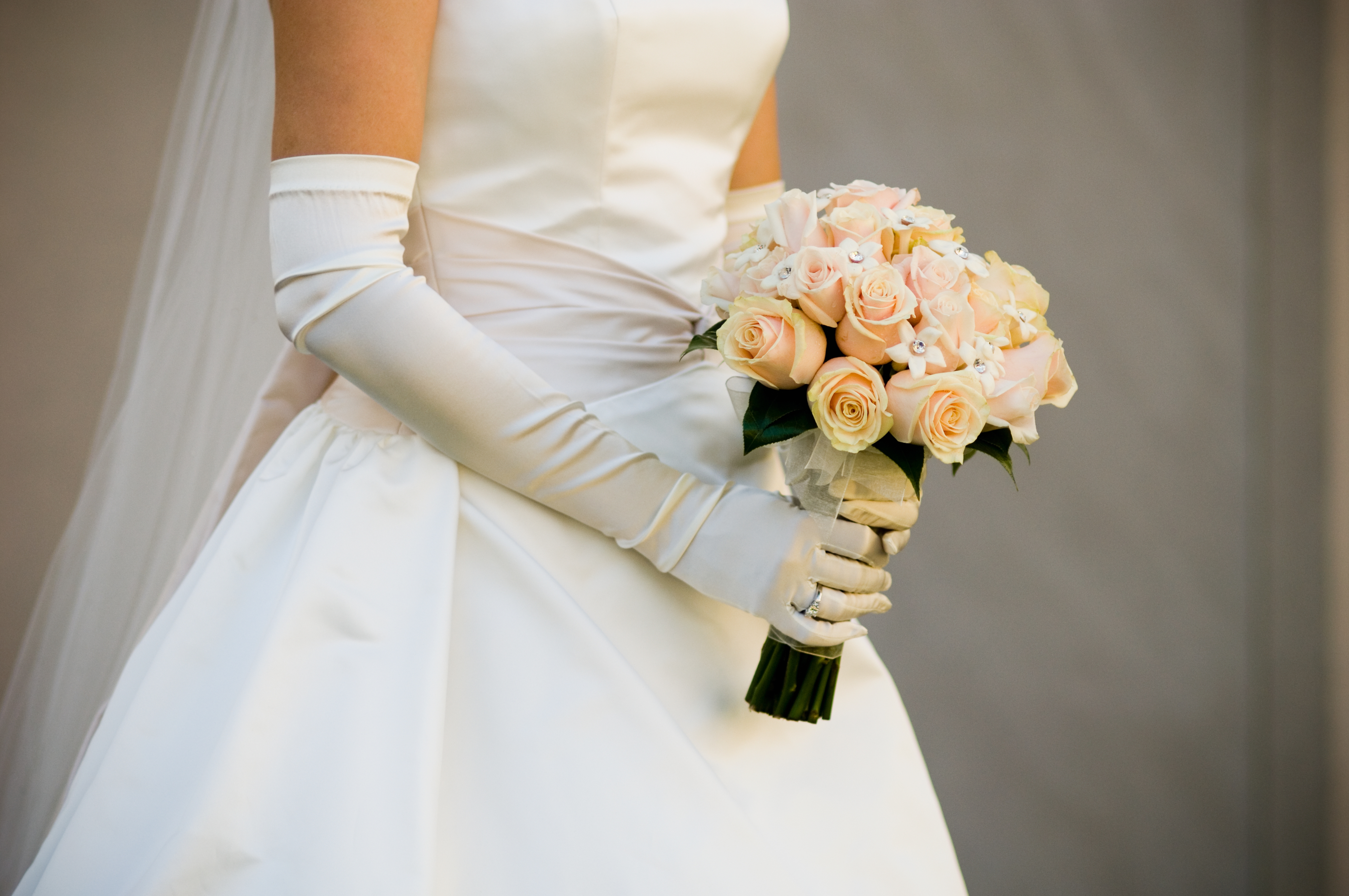 Bride in an elegant wedding dress holds a bouquet of roses, wearing long satin gloves