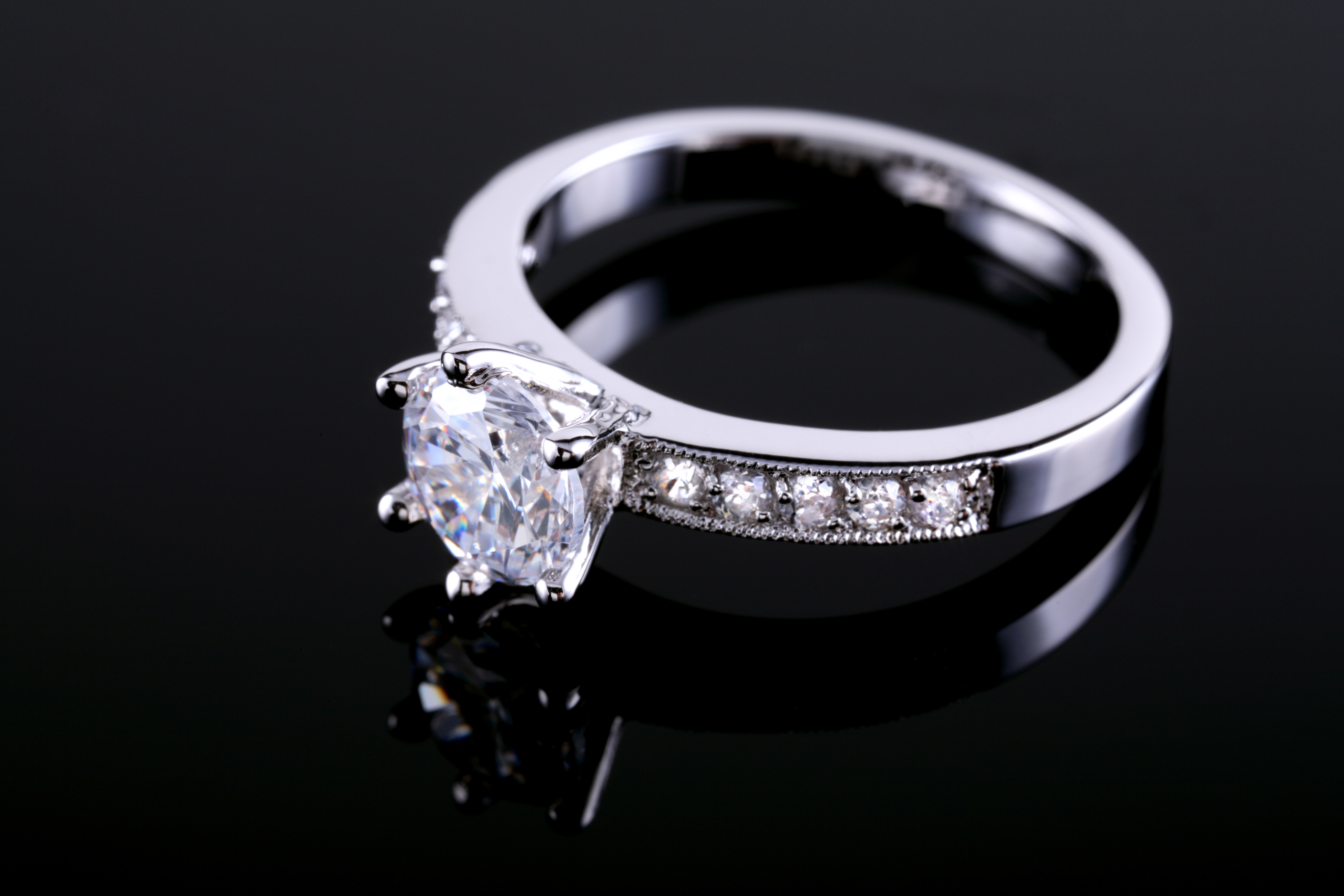 Elegant engagement ring with a large central diamond and a band adorned with smaller diamonds, showcased on a black background
