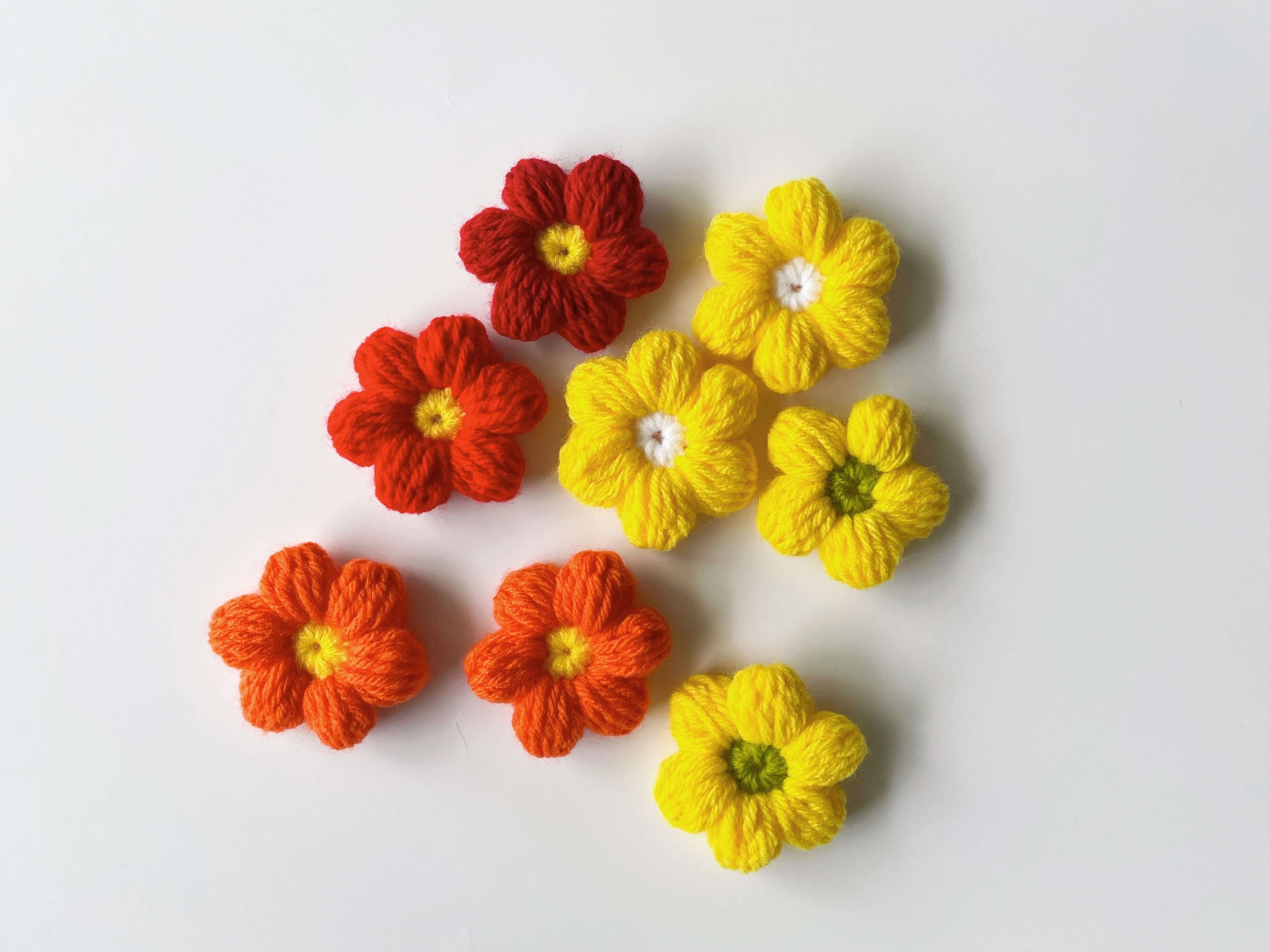 Crocheted flowers arranged on a white surface, featuring different shades and styles, suitable for wedding decor or craft inspiration