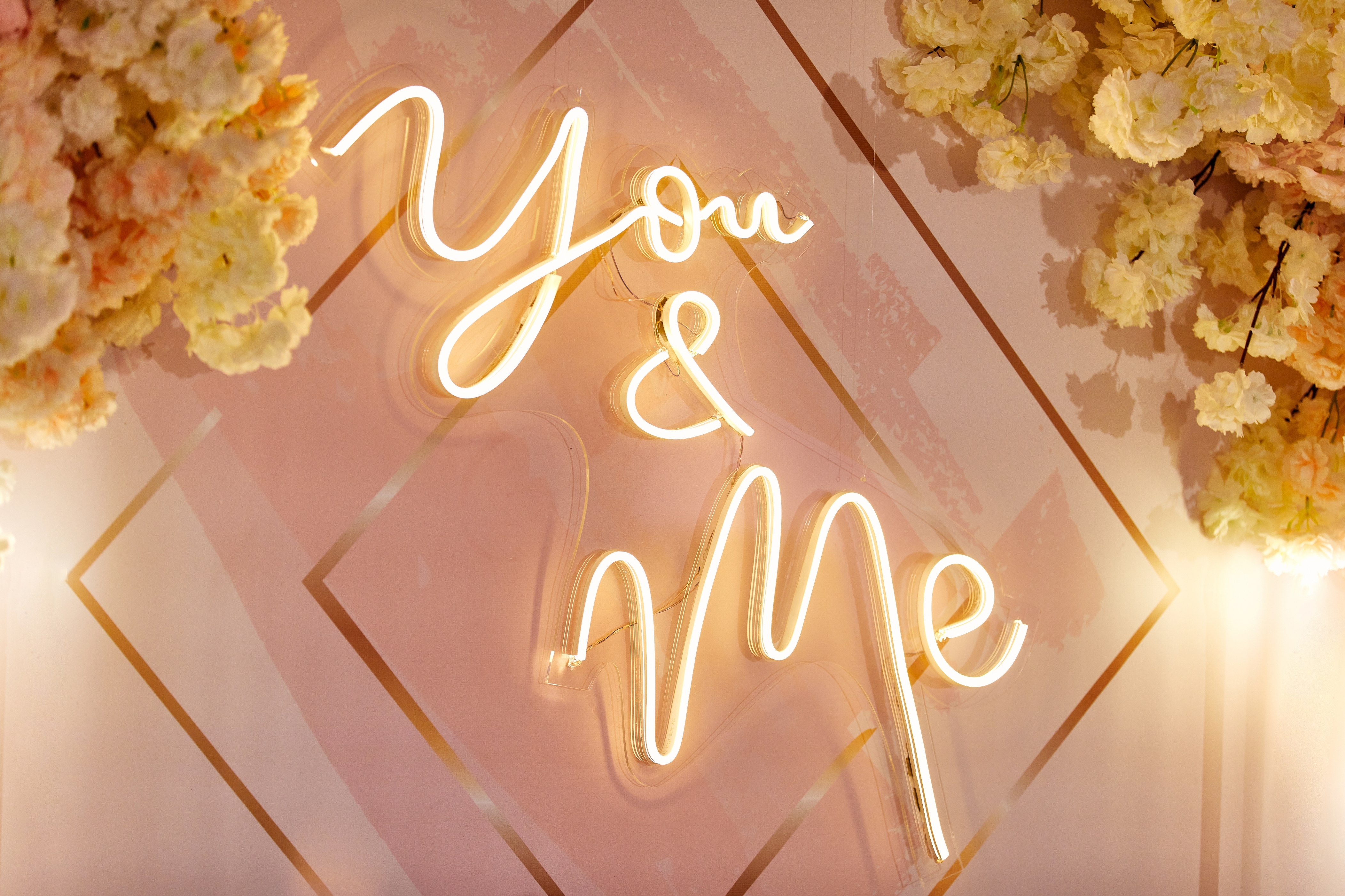 Neon sign reads "You & Me" surrounded by floral decor, creating a romantic wedding ambiance