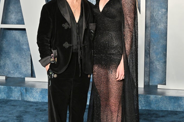 Joe Jonas and Sophie Turner on a red carpet, one in a black suit with floral designs, the other in a sheer, sparkling gown with cape sleeves
