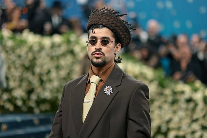 Celebrity in a stylish suit with unique hat and sunglasses poses at a formal event